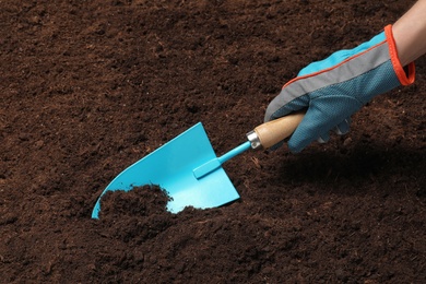 Photo of Woman digging soil with metal gardening trowel, closeup