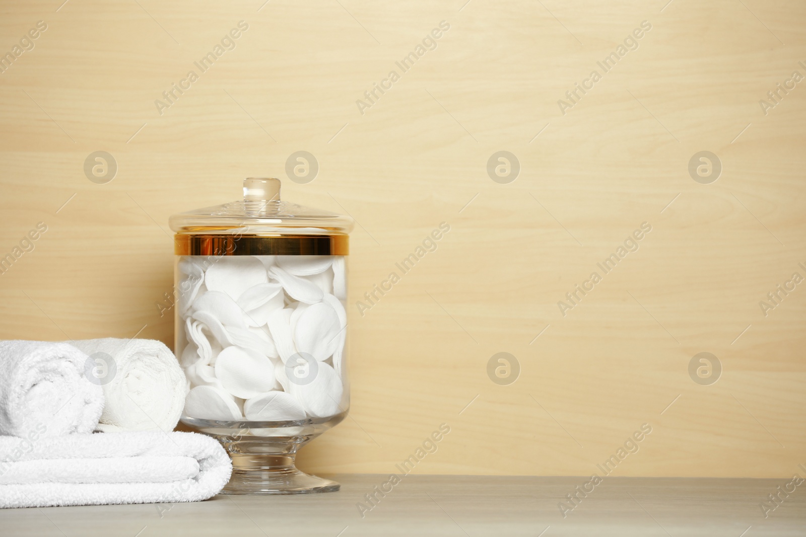 Photo of Composition of glass jar with cotton pads on table near light wooden wall. Space for text