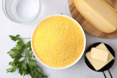 Photo of Raw cornmeal in bowl, water, cheese, parsley and butter on light table, flat lay
