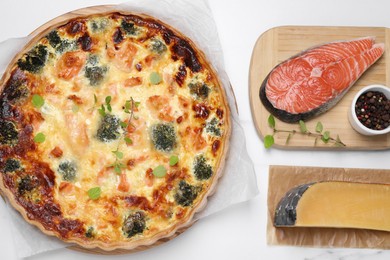 Delicious homemade quiche and ingredients on white marble table, flat lay