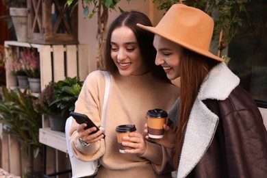 Photo of Happy friends with smartphone and paper cups outdoors