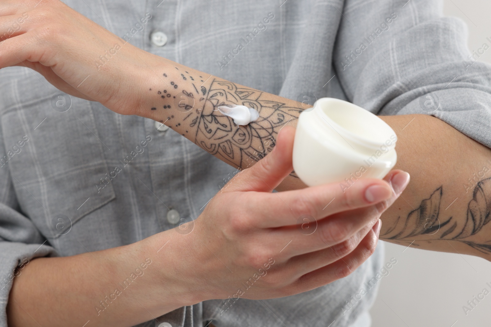 Photo of Tattooed woman with jar of cream on light background, closeup