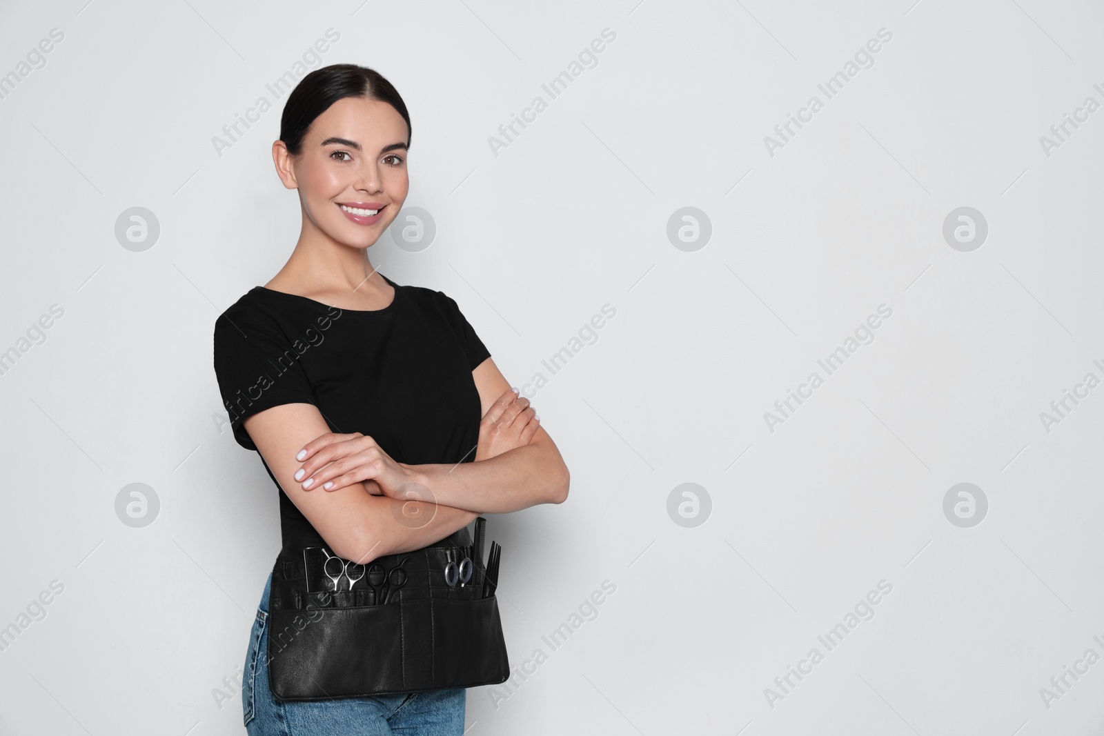 Photo of Portrait of happy hairdresser with professional tools on light background, space for text