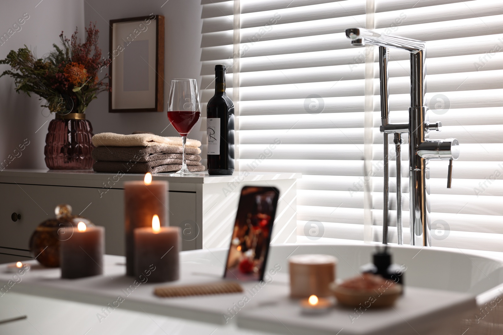 Photo of Bottle of wine, towels and flowers on chest of drawers in bathroom, selective focus