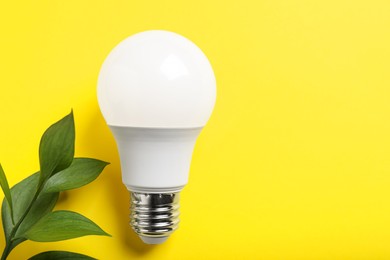 Photo of Light bulb and branch with green leaves on yellow background, flat lay. Space for text