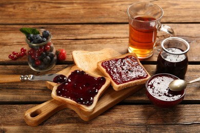 Delicious toasts served with different jams, tea and berries on wooden table