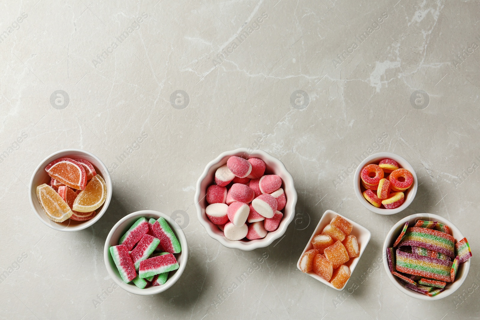 Photo of Flat lay composition with bowls of different jelly candies on light marble background. Space for text