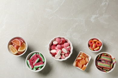Flat lay composition with bowls of different jelly candies on light marble background. Space for text