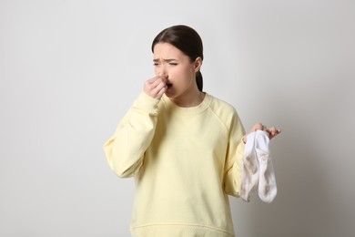 Young woman feeling bad smell from dirty socks on light grey background