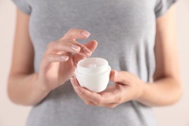 Young woman holding jar of cream on light background, closeup