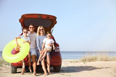 Happy family with inflatable ring near car at beach on sunny day