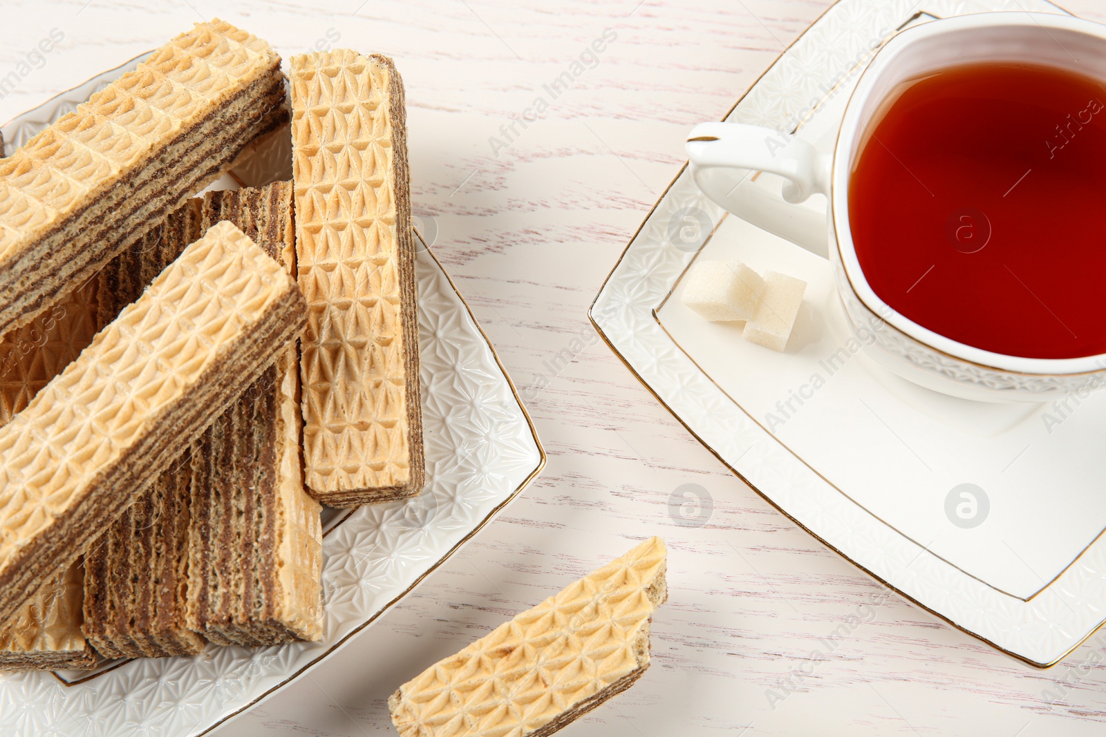 Photo of Plate of delicious wafers with cup of tea on white wooden background, closeup