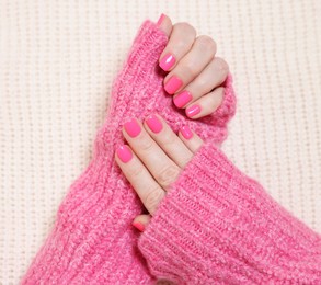 Photo of Woman showing her manicured hands with pink nail polish on knitted blanket, top view