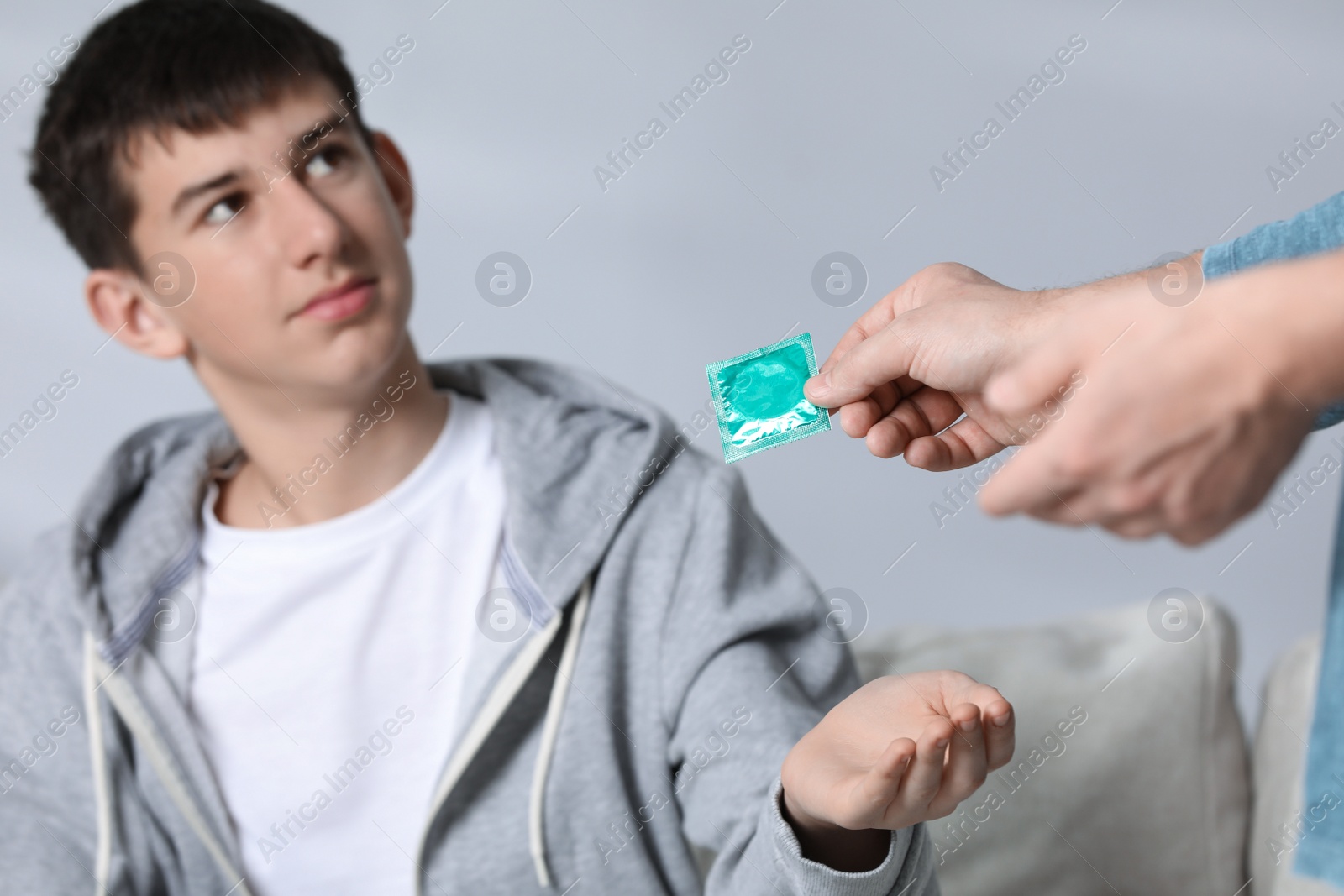 Photo of Father giving condom to his teenage son at home, closeup. Sex education concept