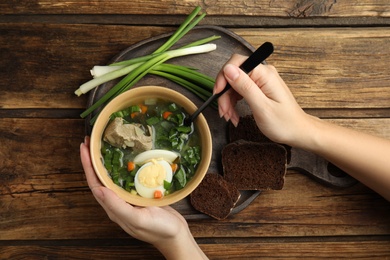 Woman eating delicious sorrel soup with meat and egg at wooden table, top view