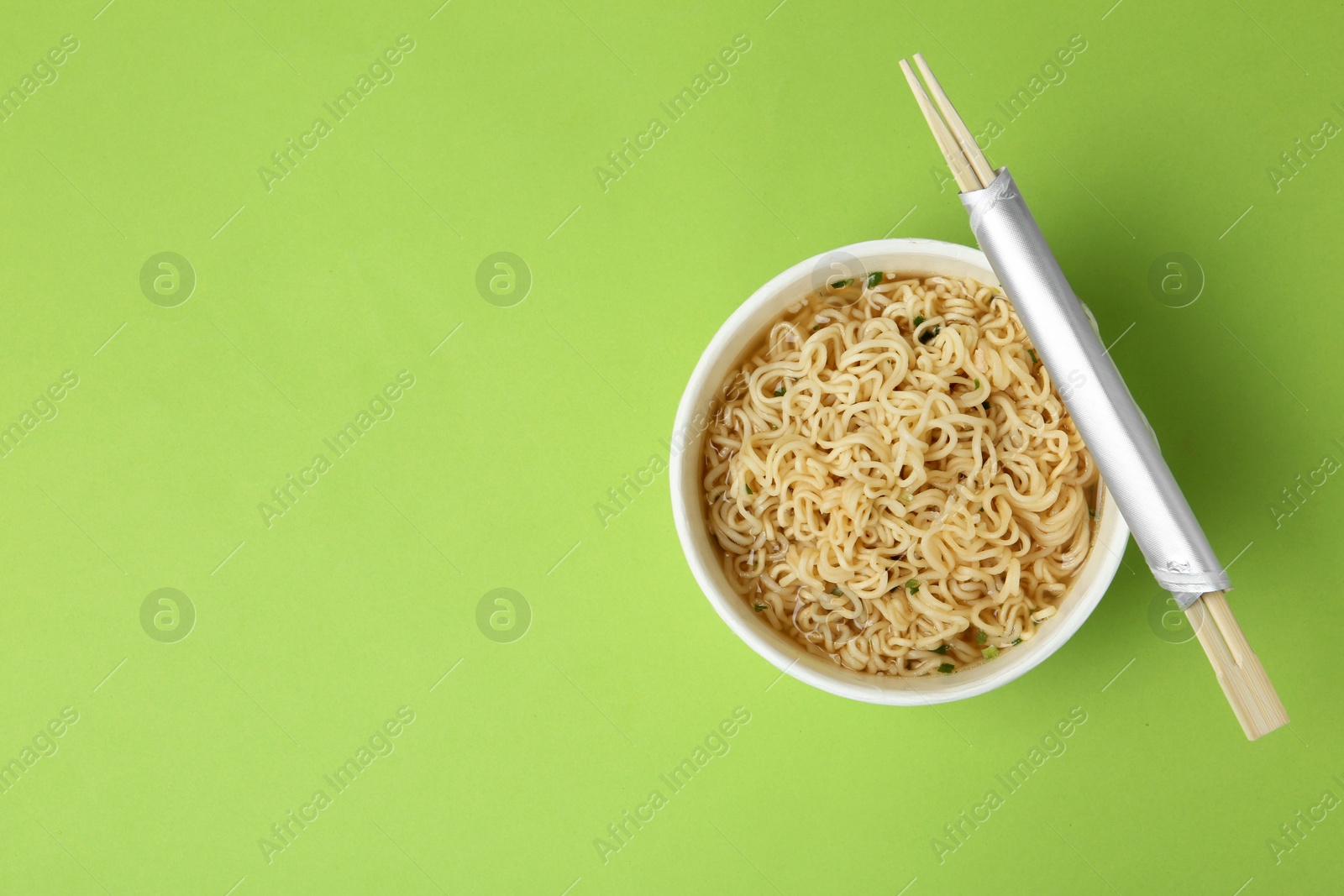 Photo of Cup of cooked instant noodles with chopsticks on color background, top view. Space for text