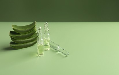 Photo of Skincare ampoules with extract of aloe vera and cut green leaves on color background. Space for text