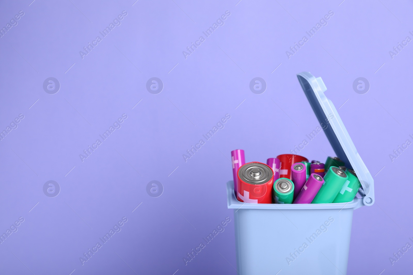 Photo of Many used batteries in recycling bin on light purple background. Space for text