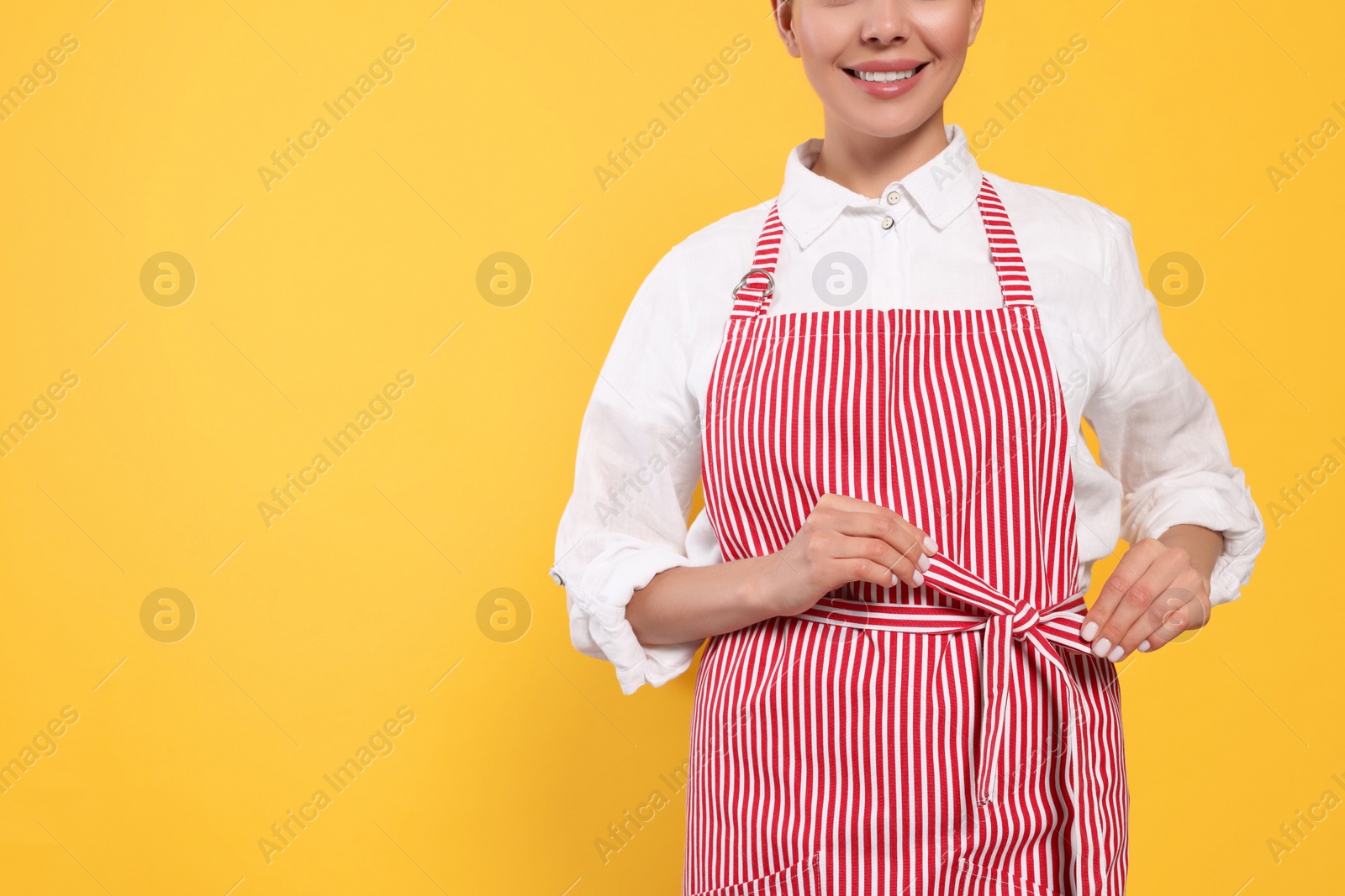 Photo of Young woman in red striped apron on yellow background, closeup. Space for text