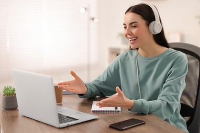 Photo of Young woman in headphones using video chat during webinar at table in room