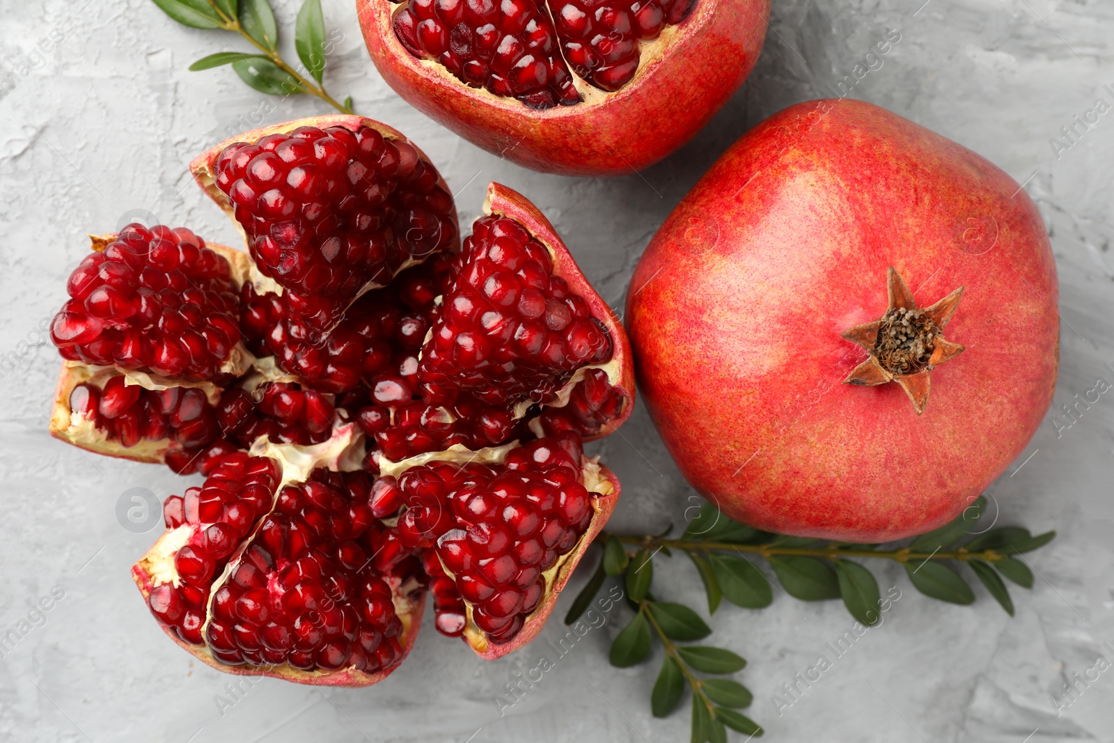 Photo of Fresh pomegranates and green leaves on grey textured table, flat lay