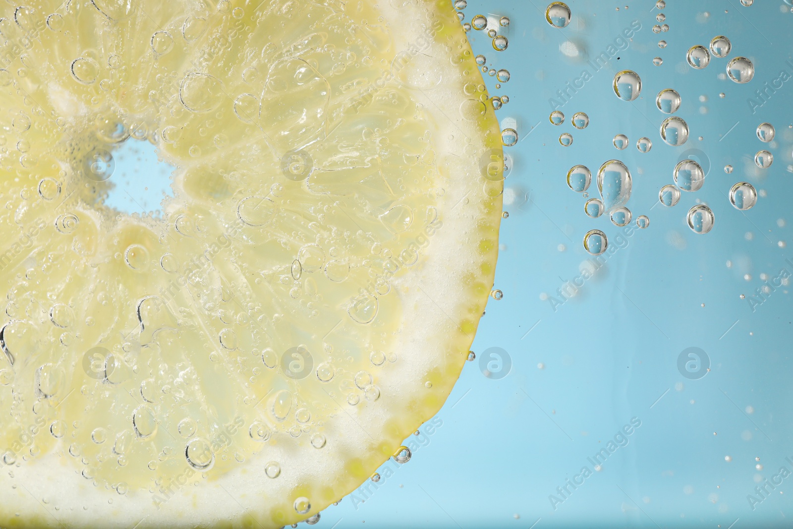 Photo of Juicy lemon slice in soda water against light blue background, closeup. Space for text