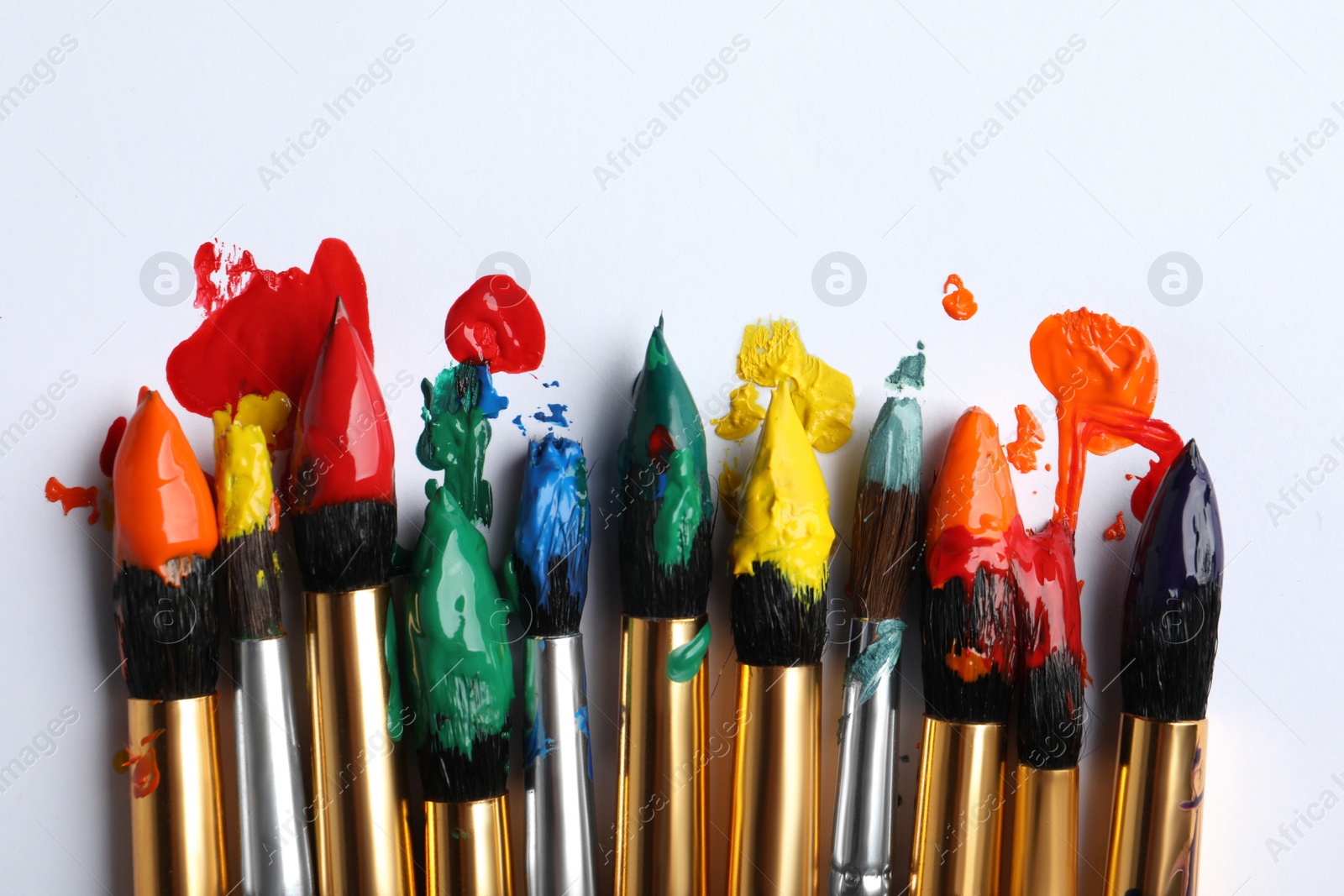 Photo of Brushes with colorful paints on white background, flat lay. Space for text