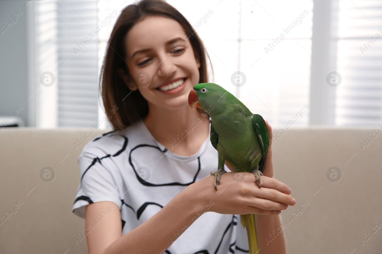 Photo of Young woman with cute Alexandrine parakeet indoors