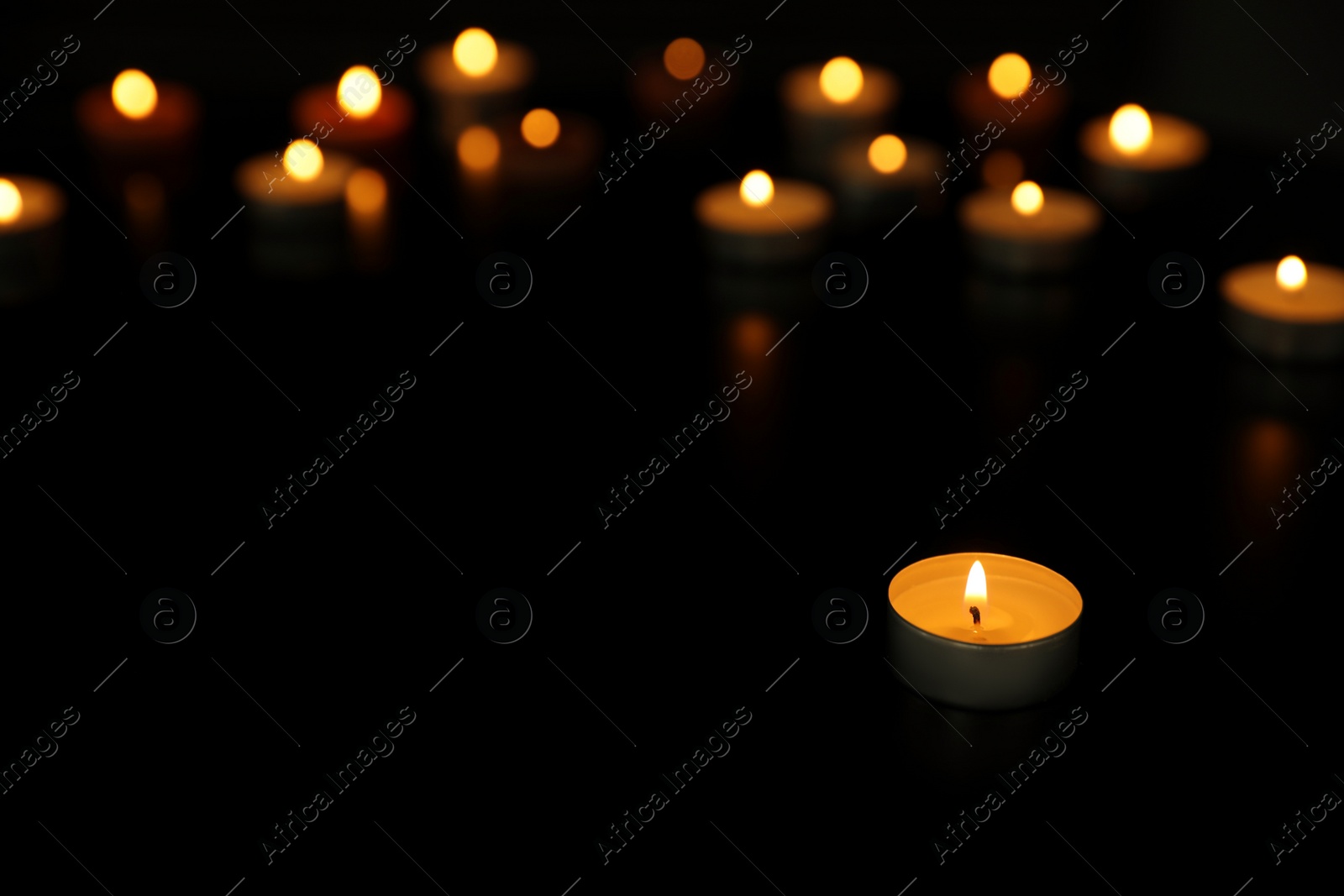 Photo of Many burning tealight candles on dark background, space for text