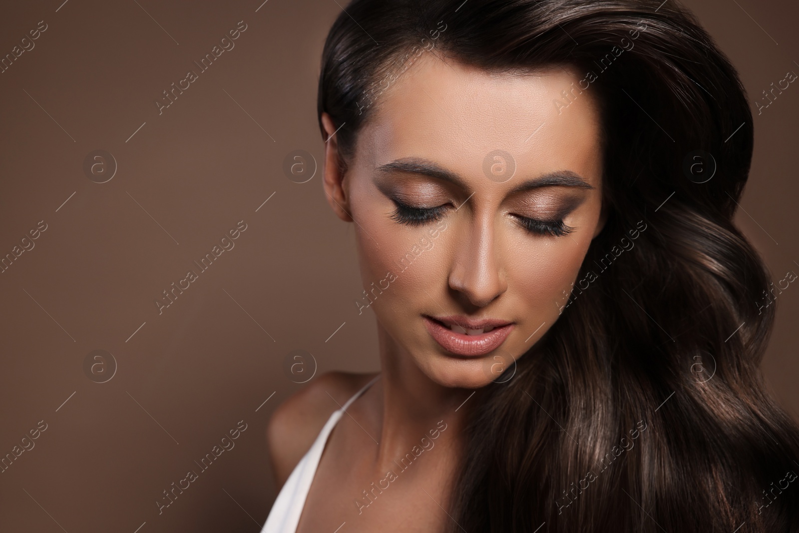 Image of Gorgeous woman with shiny wavy hair on brown background, space for text. Professional hairstyling