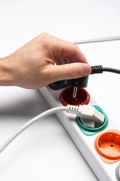 Photo of Man inserting power plug into extension cord on white background, closeup. Electrician's professional equipment