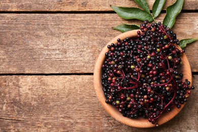 Bowl with tasty elderberries (Sambucus) on wooden table, top view. Space for text