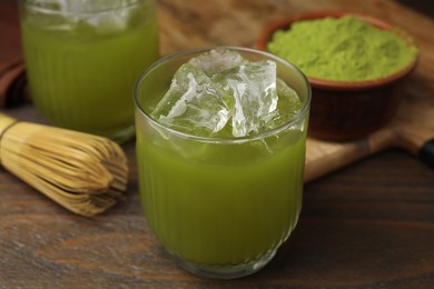 Photo of Glass of delicious iced green matcha tea, powder and bamboo whisk on wooden table, closeup