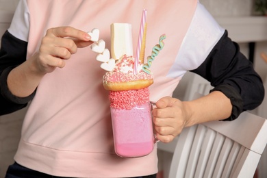Photo of Woman holding mason jar of tasty milk shake with sweets indoors, closeup