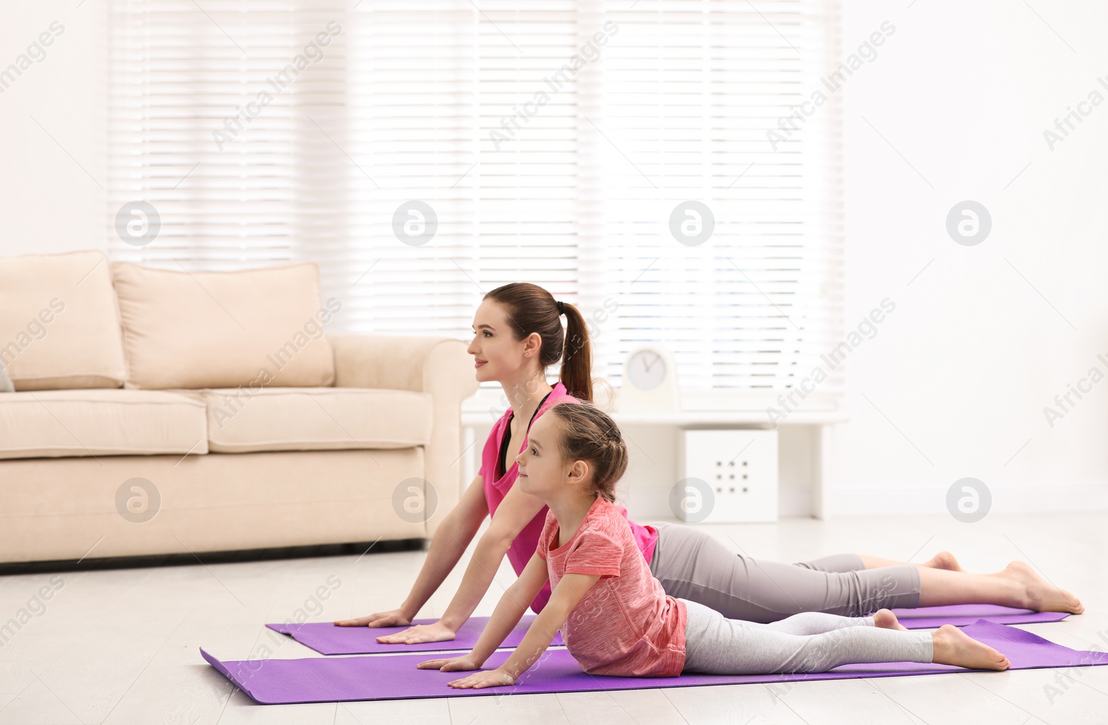 Photo of Young mother with little daughter practicing yoga at home