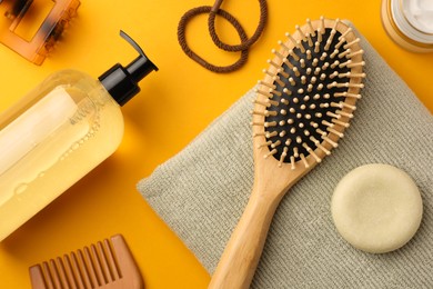 Photo of Wooden brush, comb and different hair products on orange background, flat lay