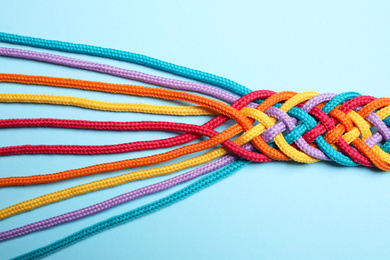 Photo of Braided colorful ropes on light blue background, top view. Unity concept