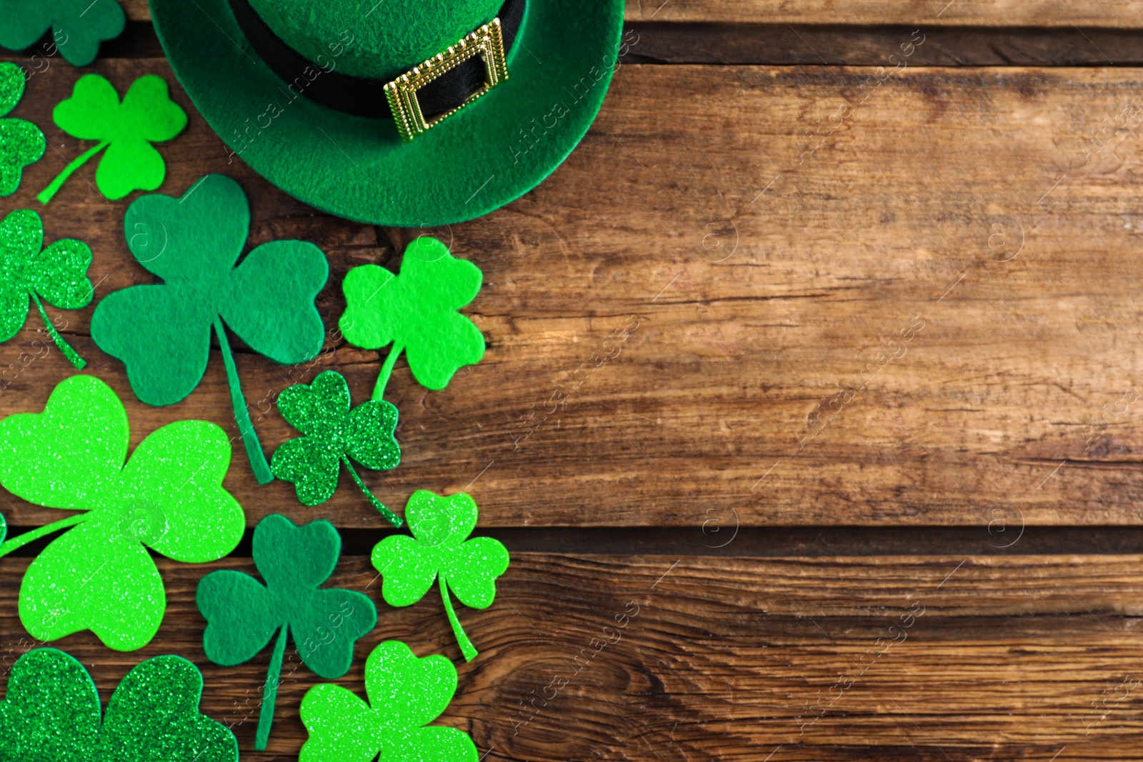Photo of Green leprechaun hat and clover leaves on wooden table, flat lay with space for text. St. Patrick's Day celebration