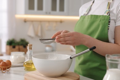Photo of Making bread. Woman sifting flour onto dough at white table in kitchen, closeup