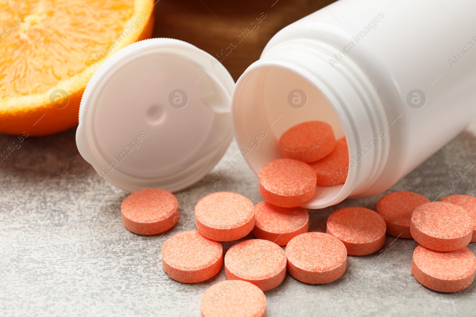 Photo of Dietary supplements. Overturned bottle, pills and orange on grey table, closeup