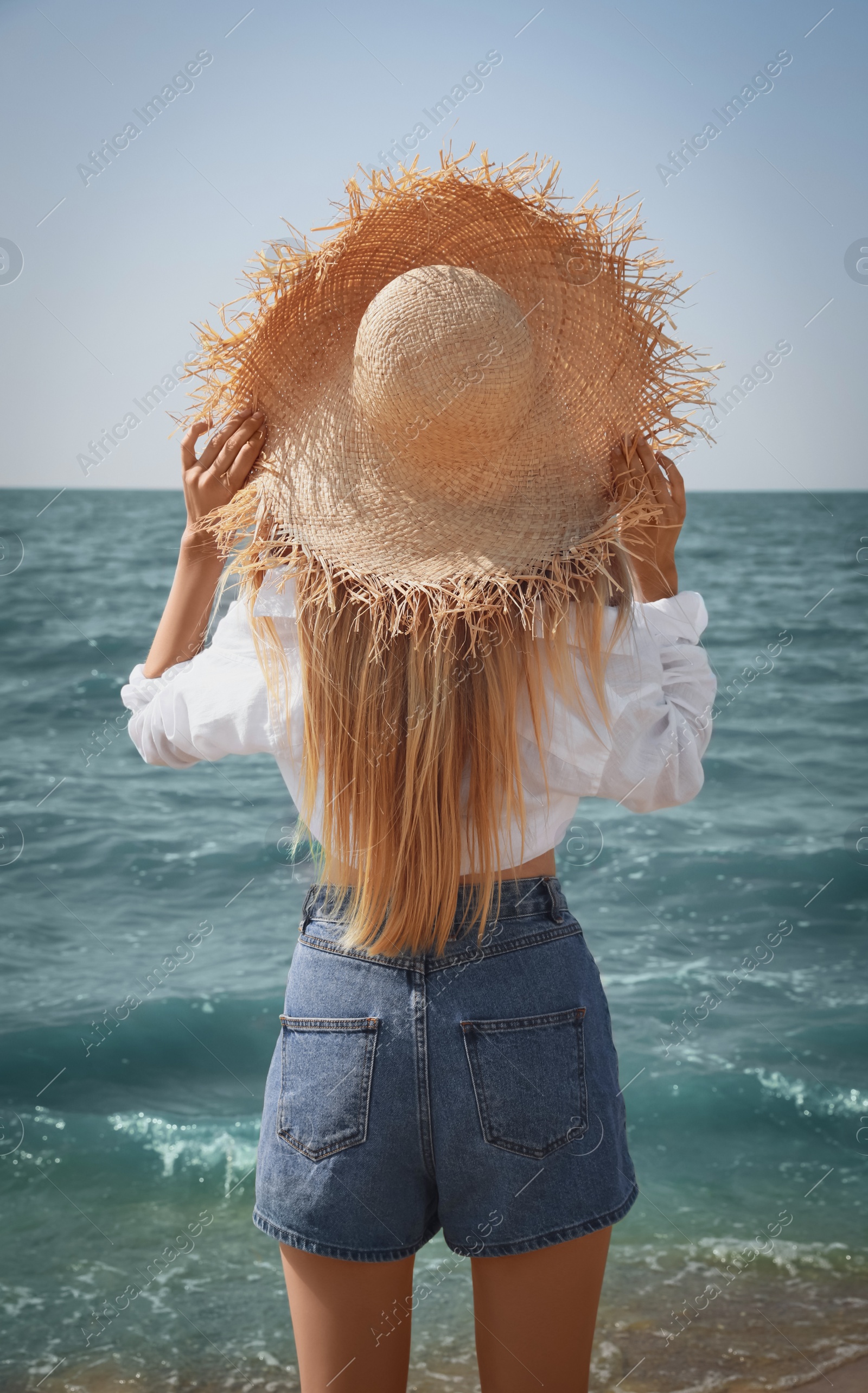 Photo of Young woman with straw hat near sea on sunny day in summer, back view