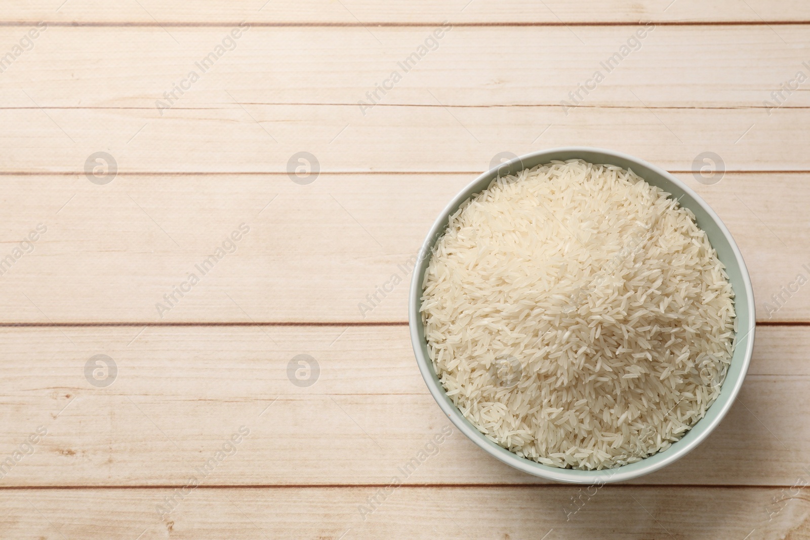 Photo of Raw basmati rice in bowl on white wooden table, top view. Space for text