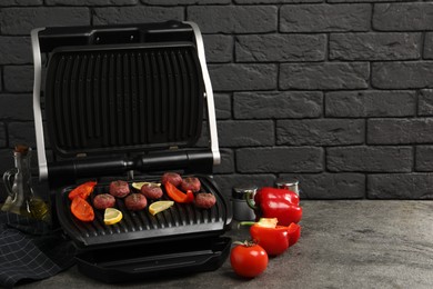 Photo of Electric grill with meat balls, bell peppers and lemon on grey textured table, space for text