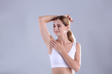 Photo of Young woman showing armpit on grey background. Using deodorant