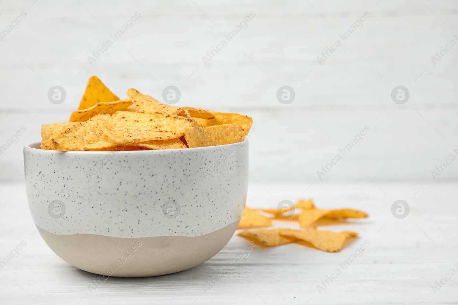 Photo of Bowl with tasty Mexican nachos chips on white wooden table, space for text