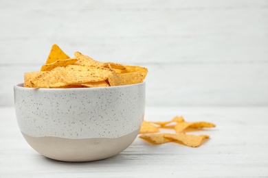 Bowl with tasty Mexican nachos chips on white wooden table, space for text