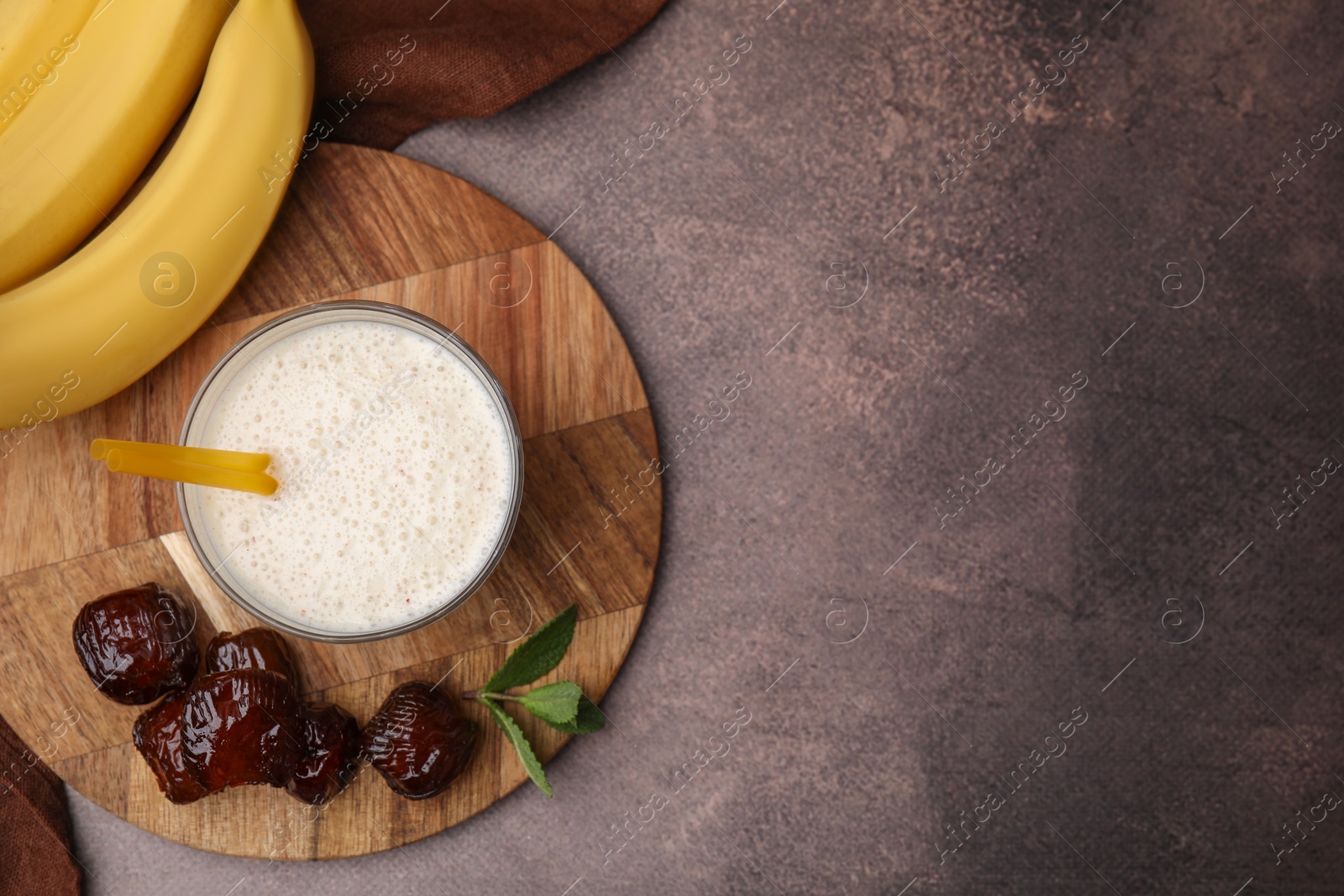 Photo of Glass of delicious date smoothie, dried fruits, mint and bananas on brown table, flat lay. Space for text