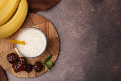 Photo of Glass of delicious date smoothie, dried fruits, mint and bananas on brown table, flat lay. Space for text