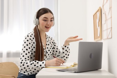 Photo of E-learning. Young woman using laptop during online lesson at table indoors