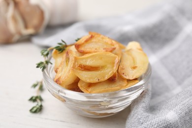 Fried garlic cloves and thyme in bowl on white table, closeup